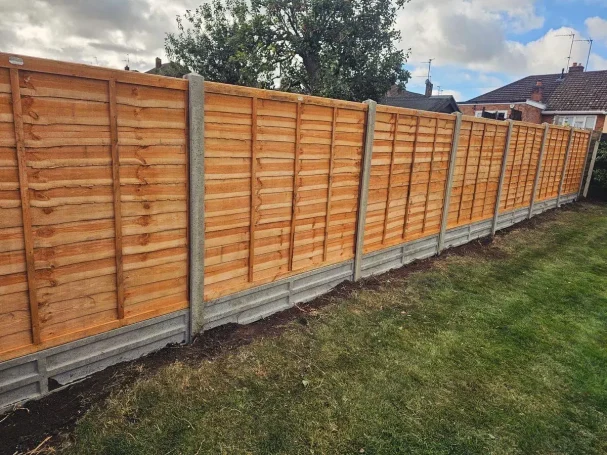 Wooden fence panels with a concrete base, set in a grassy garden area.