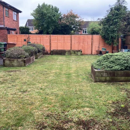 Back garden with trimmed lawn, raised flower beds, and a wooden fence in the background.