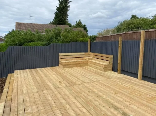 Wooden deck area with seating, surrounded by fencing and greenery.