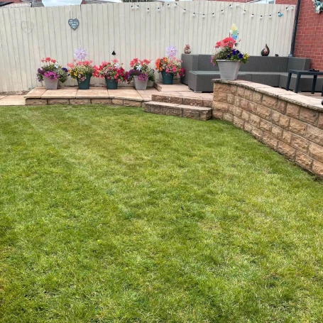 Neatly manicured lawn with flower pots and a stone wall in a garden setting.