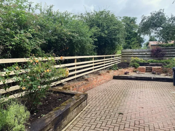 A garden with a wooden fence, flowering plants, and paved pathway.