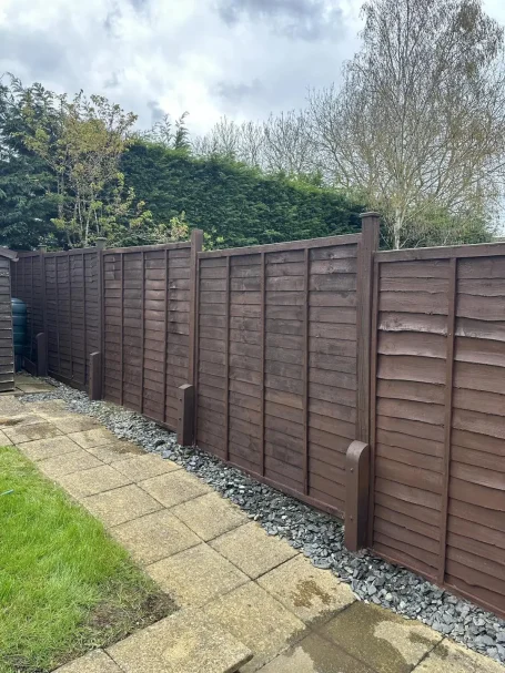  wooden fence along a pathway, with grass and stones on either side, under a cloudy sky.