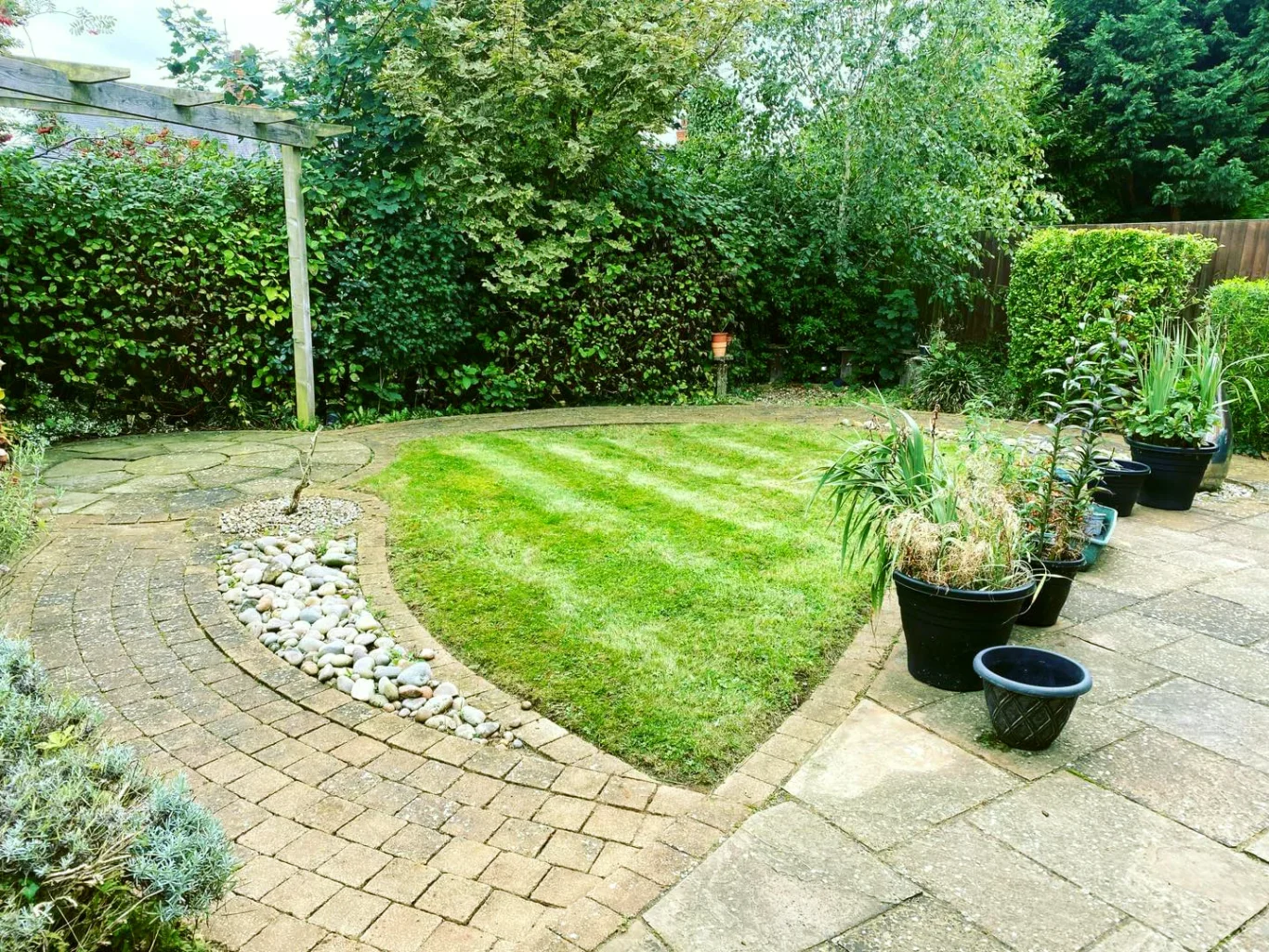A landscaped garden with striped lawn and potted plants along stone paths.