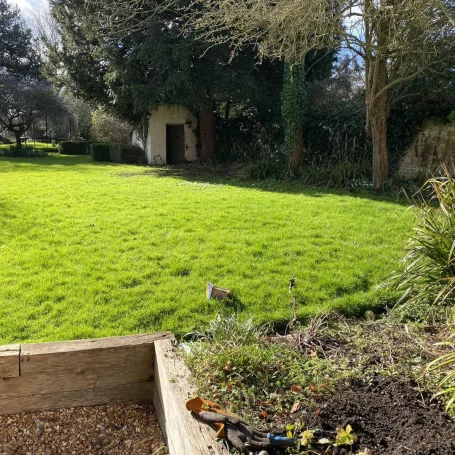 Lush green garden with a wooden planter and a view of a small building in the background.