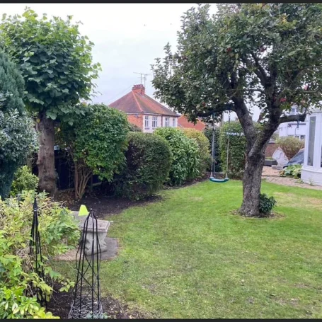 Garden scene with neatly trimmed hedges, trees, and a swing set.