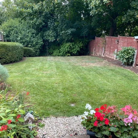 A well-maintained garden with green grass, flower beds, and a brick wall backdrop.