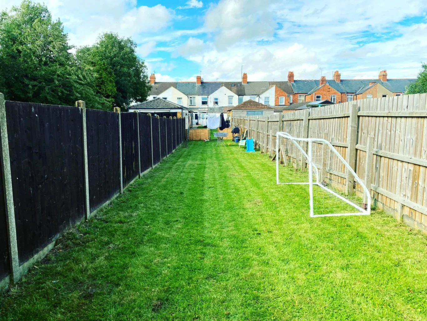 Narrow grass lane with a white goalpost and wooden fences on either side.