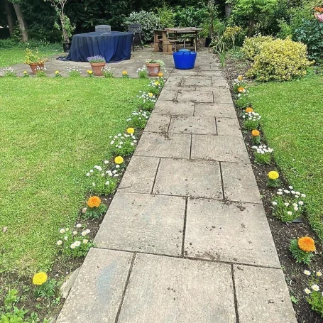 A stone pathway lined with flowers, leading to a garden seating area.
